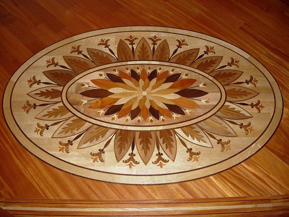 Intricato intarsio sul pavimento in parquet di legno con motivi floreali e fogliari in varie tonalità di marrone e beige.