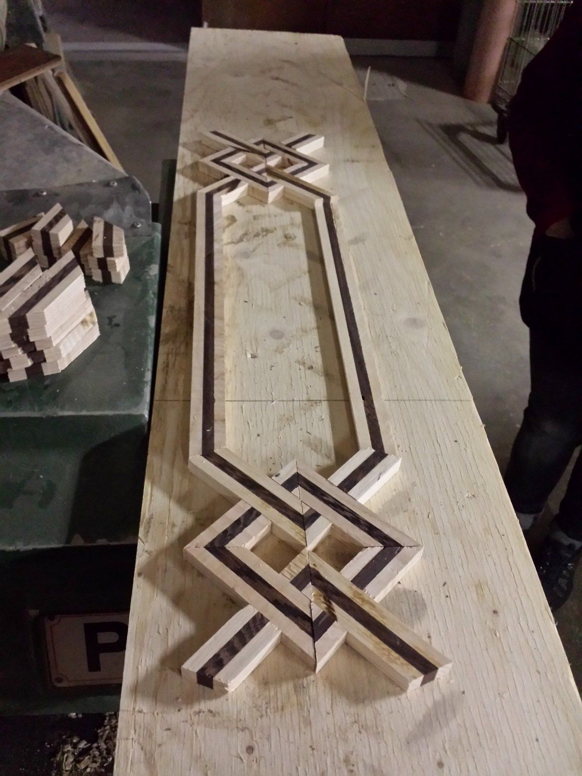 Intarsio decorativo in legno, disegno geometrico. Legno chiaro con strisce scure, posizionato su una superficie in legno chiaro.