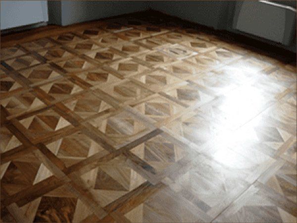 Pavimento in parquet con motivo geometrico che riflette la luce intensa.
