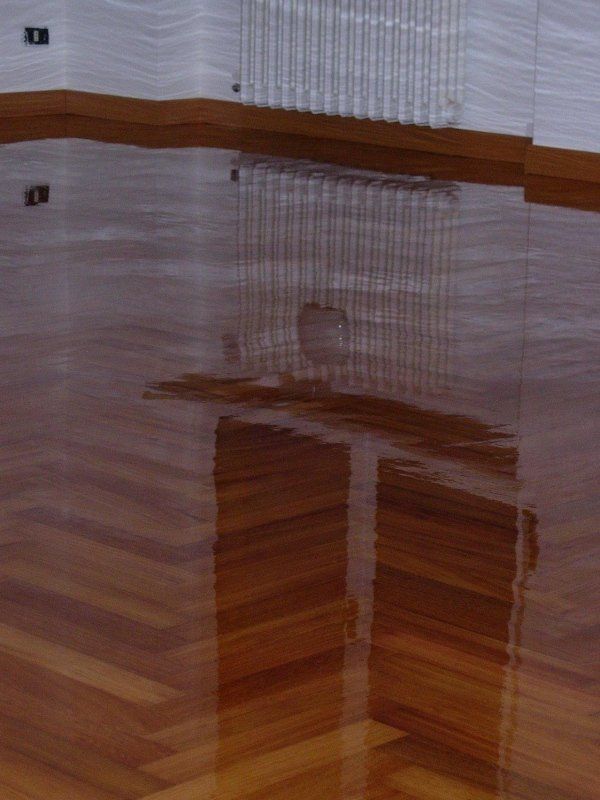 Pavimento in legno lucido e riflettente. Sono visibili i riflessi delle pareti e degli oggetti.