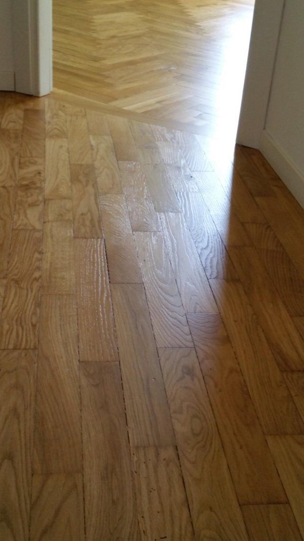 Pavimento in legno con parquet e assi rettangolari. La luce intensa filtra dalla porta.