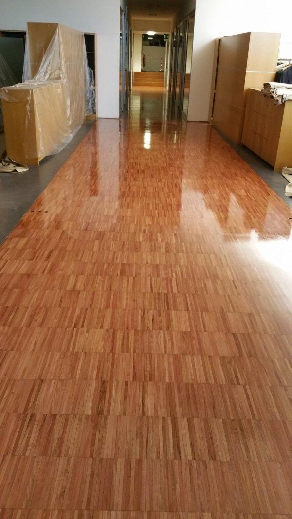 Pavimento in parquet lucido e rosso in un corridoio, che riflette la luce, con scatole di cartone e armadietti.