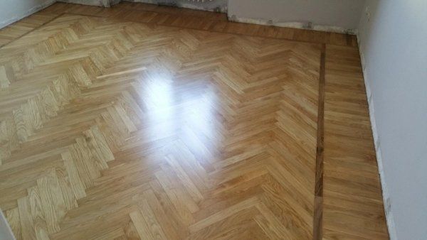 Pavimento in legno con motivo a spina di pesce e finitura lucida, che riflette la luce.
