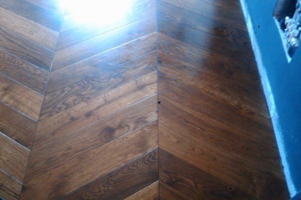 Pavimento in legno scuro con motivo a zig-zag. Angolo con parete blu sulla destra.