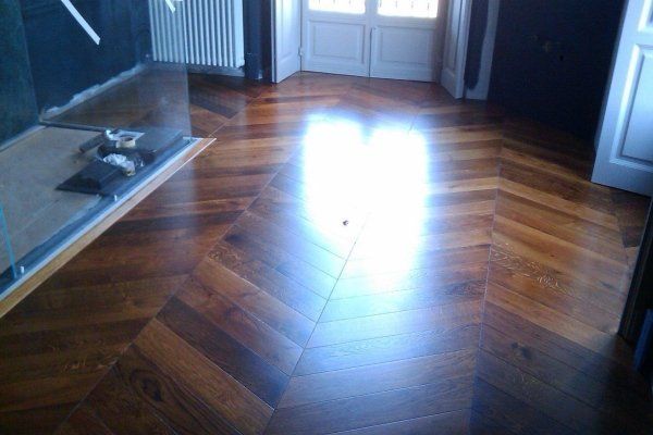 Un pavimento in legno lucido con motivo a spina di pesce. La luce si riflette sulla superficie.