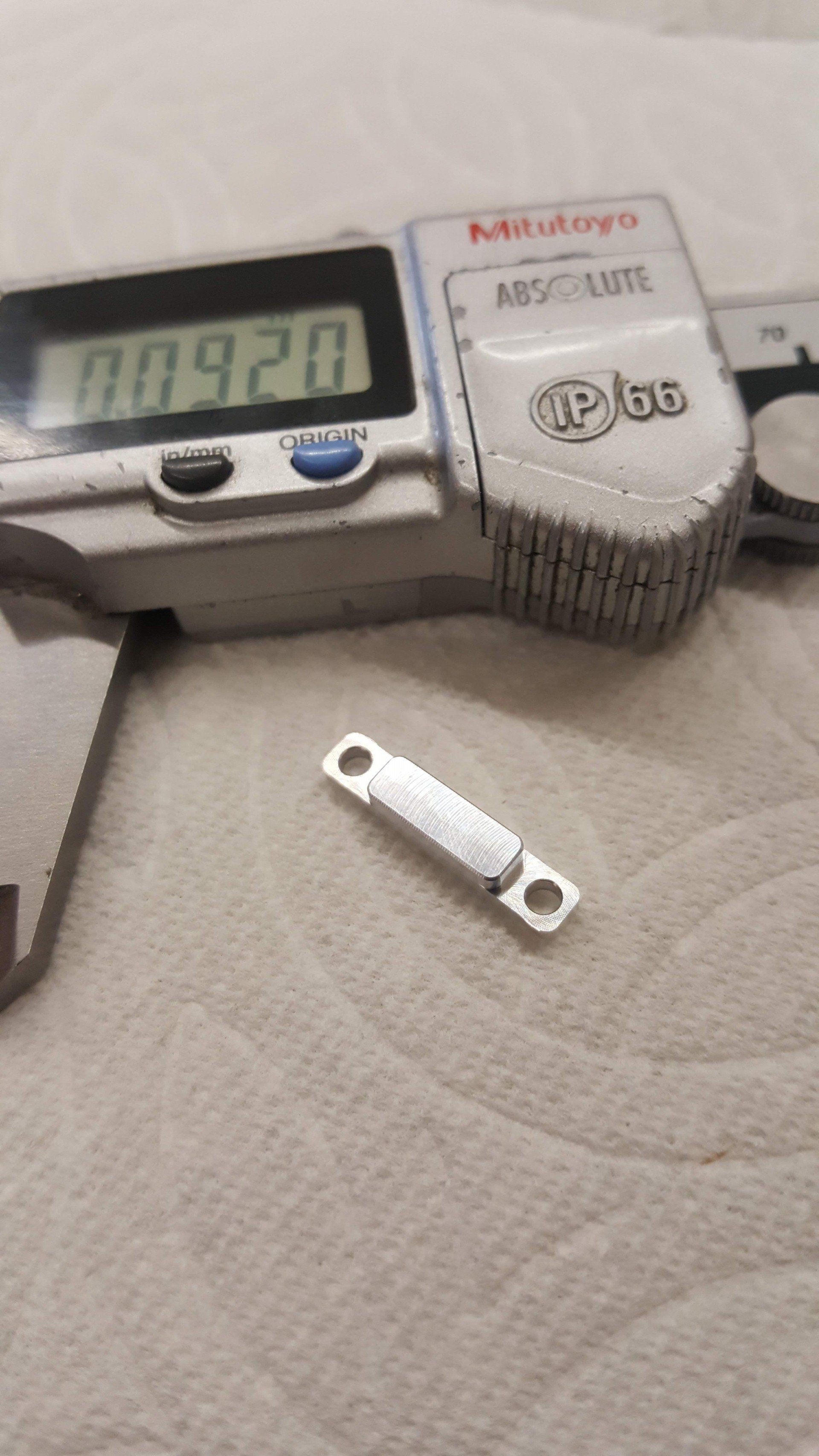 A digital caliper is sitting on a table next to a piece of metal.