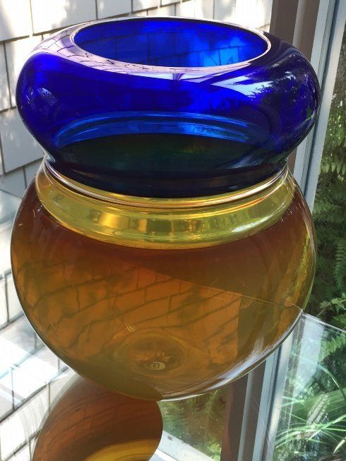 A blue and gold vase is sitting on a table in front of a window.