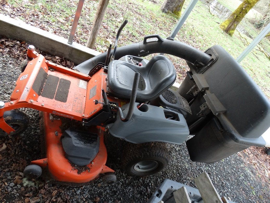 A lawn mower is sitting on the ground next to a trash can.