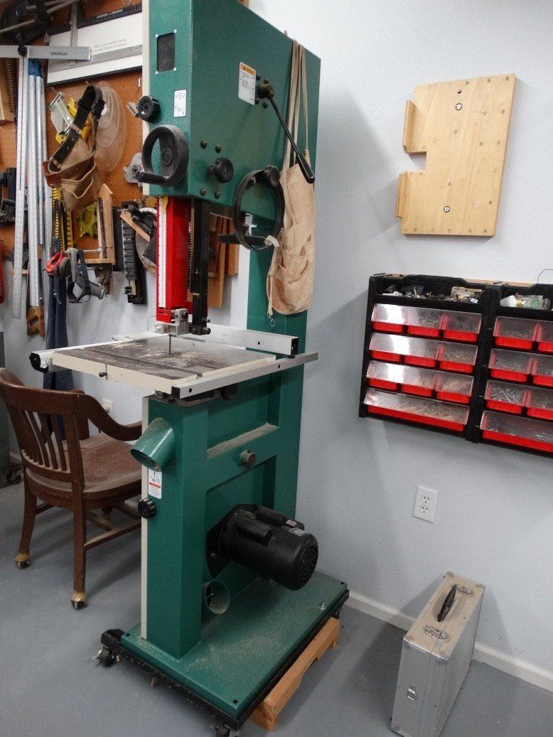 A green band saw is sitting in a room next to a chair