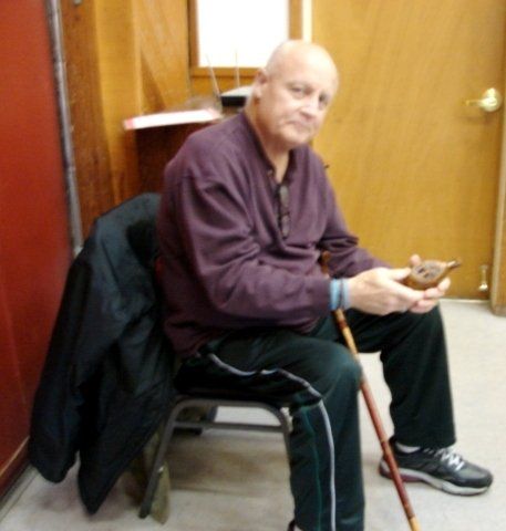 A man with a cane is sitting in a chair looking at his phone