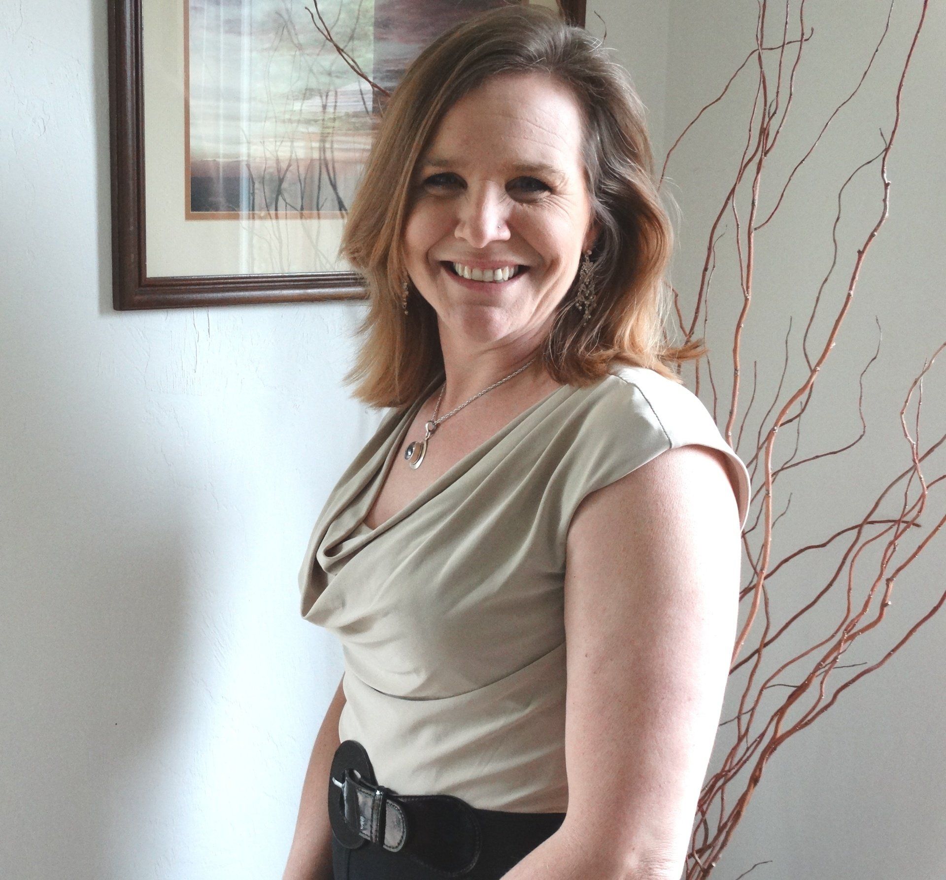 A woman is smiling in front of a picture on the wall