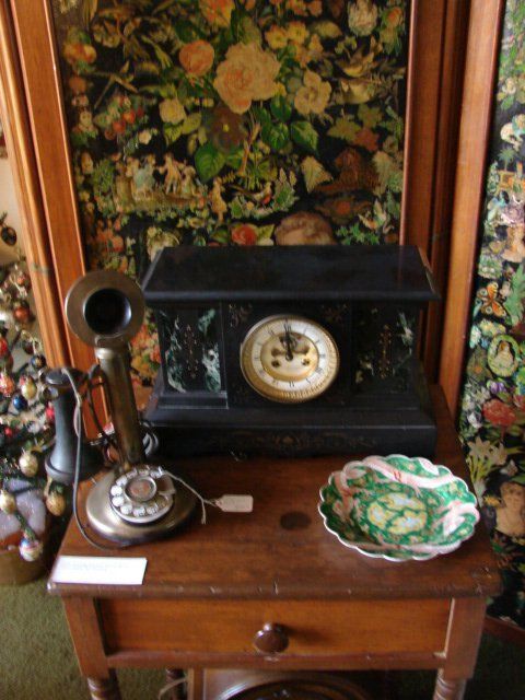 A clock sits on a wooden table next to a phone and a plate
