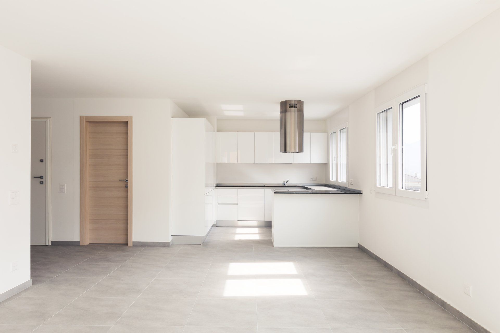An empty living room with a kitchen in the background.