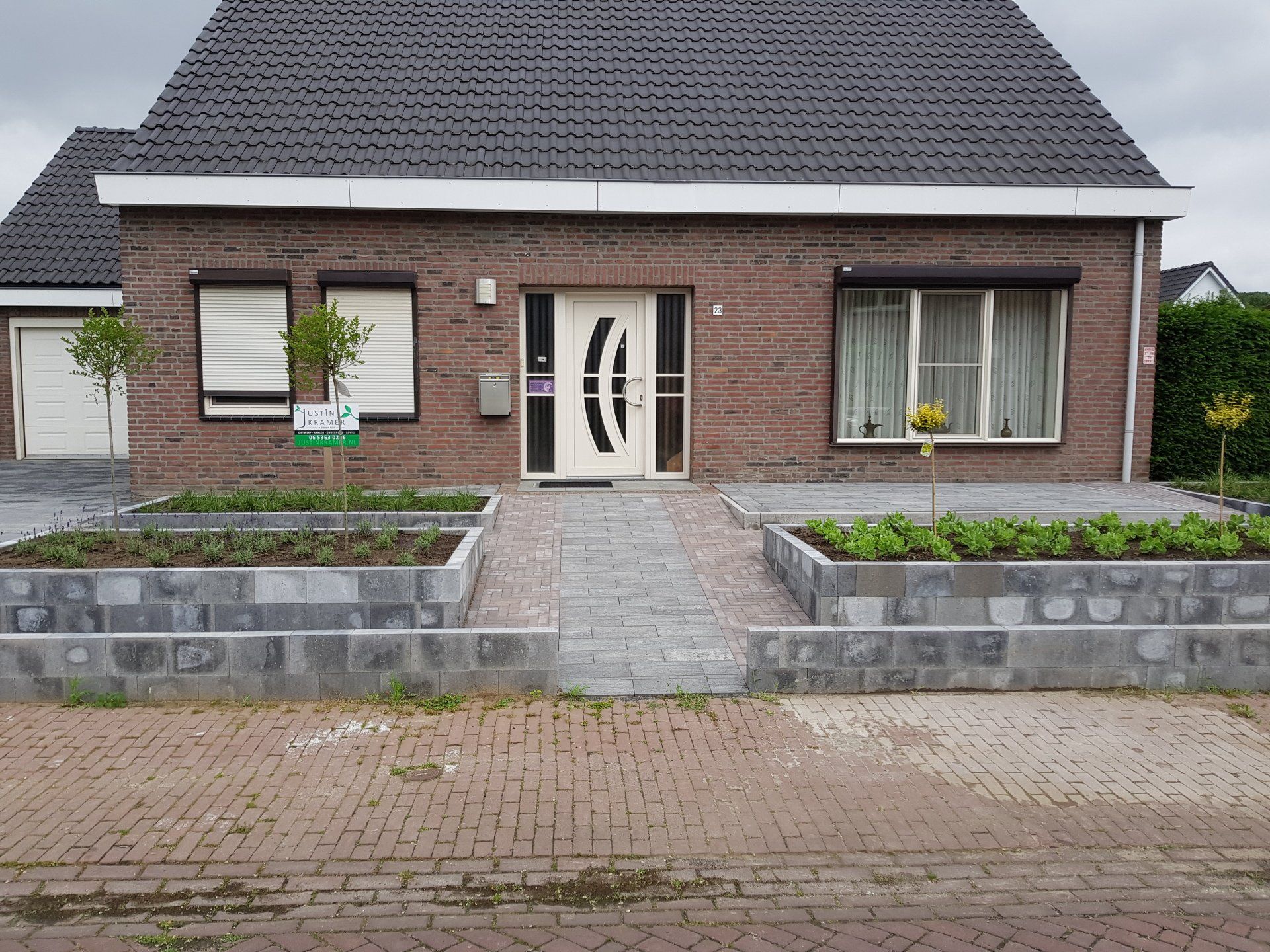 Bakstenen huis met een pannendak, bloembedden in de voortuin en een centraal pad naar de voordeur.