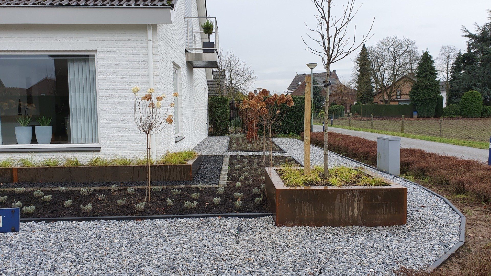 Moderne woning met een grindpad, verhoogde plantenbakken en een kleine boom in een aangelegde tuin.