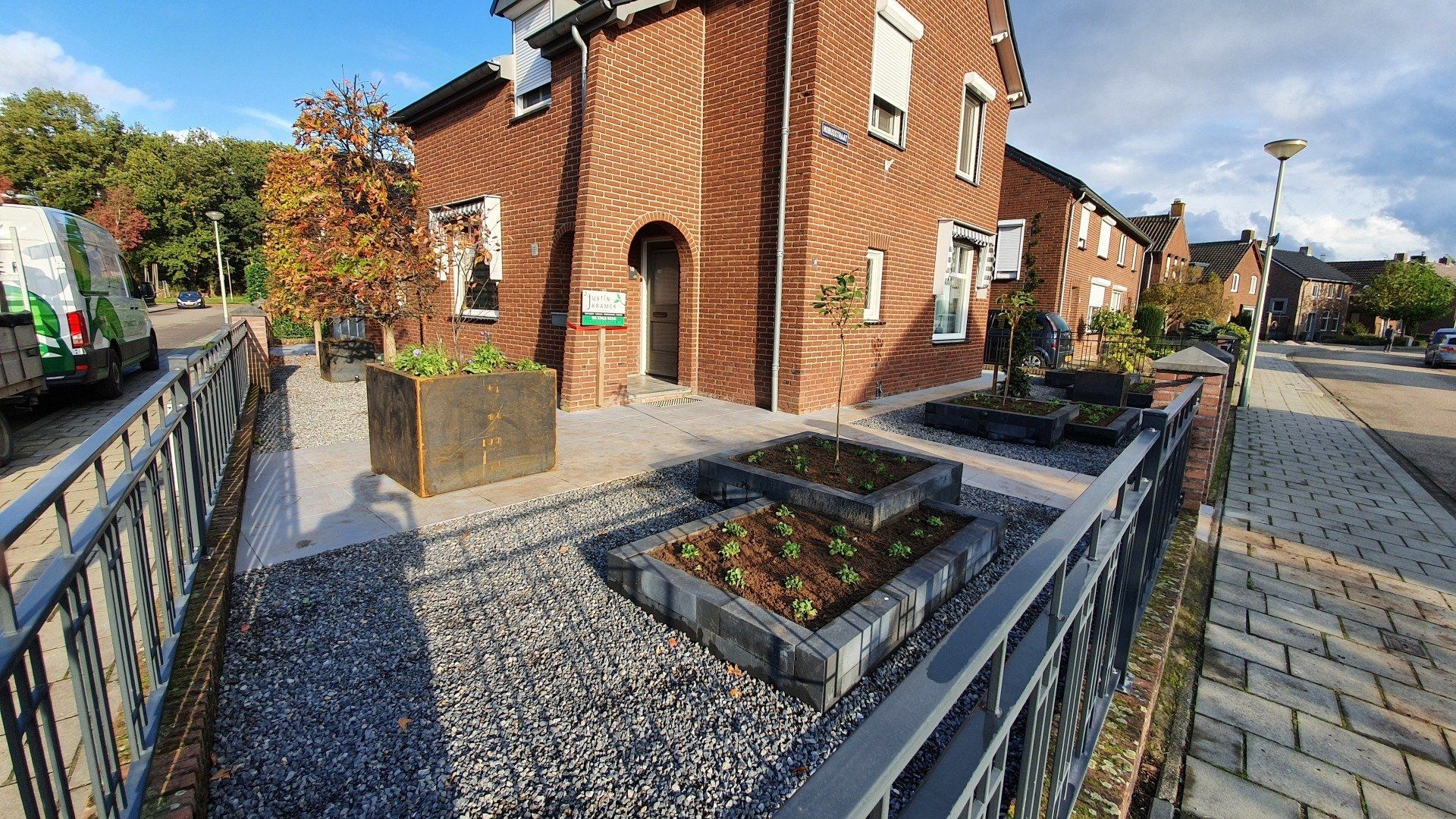 Bakstenen huis naast een grindtuin met verhoogde plantenbakken aan een woonstraat
