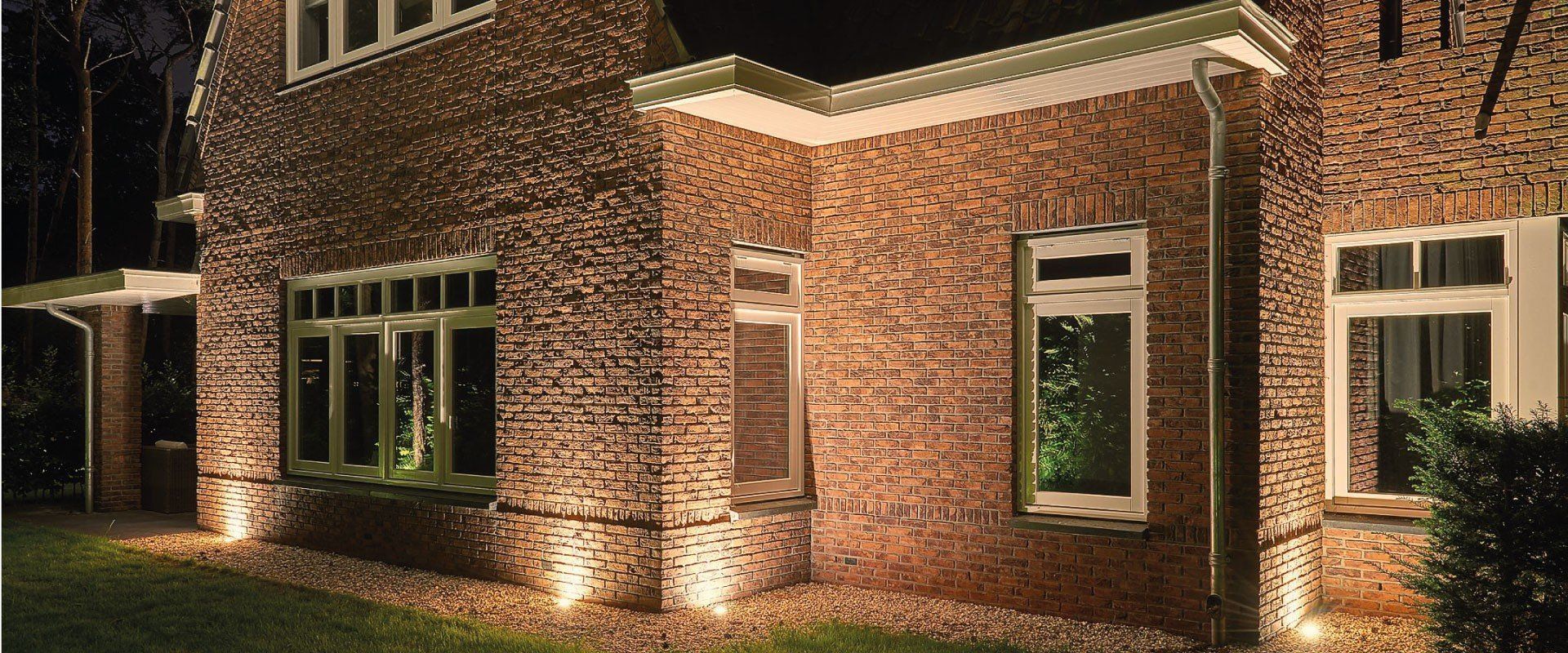 De buitenkant van het bakstenen gebouw wordt 's nachts verlicht door warme grondspots.