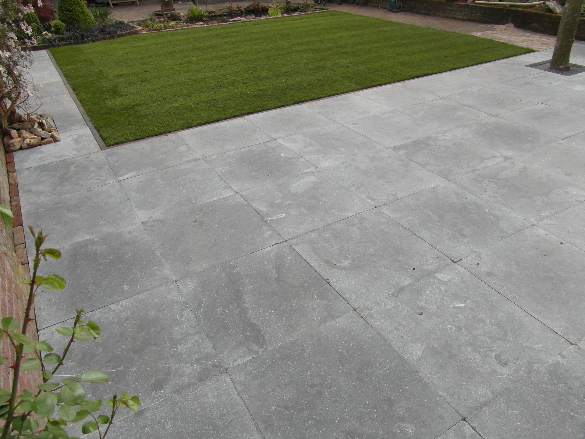 Een betonnen terras naast een groen gazon in een aangelegde tuin.