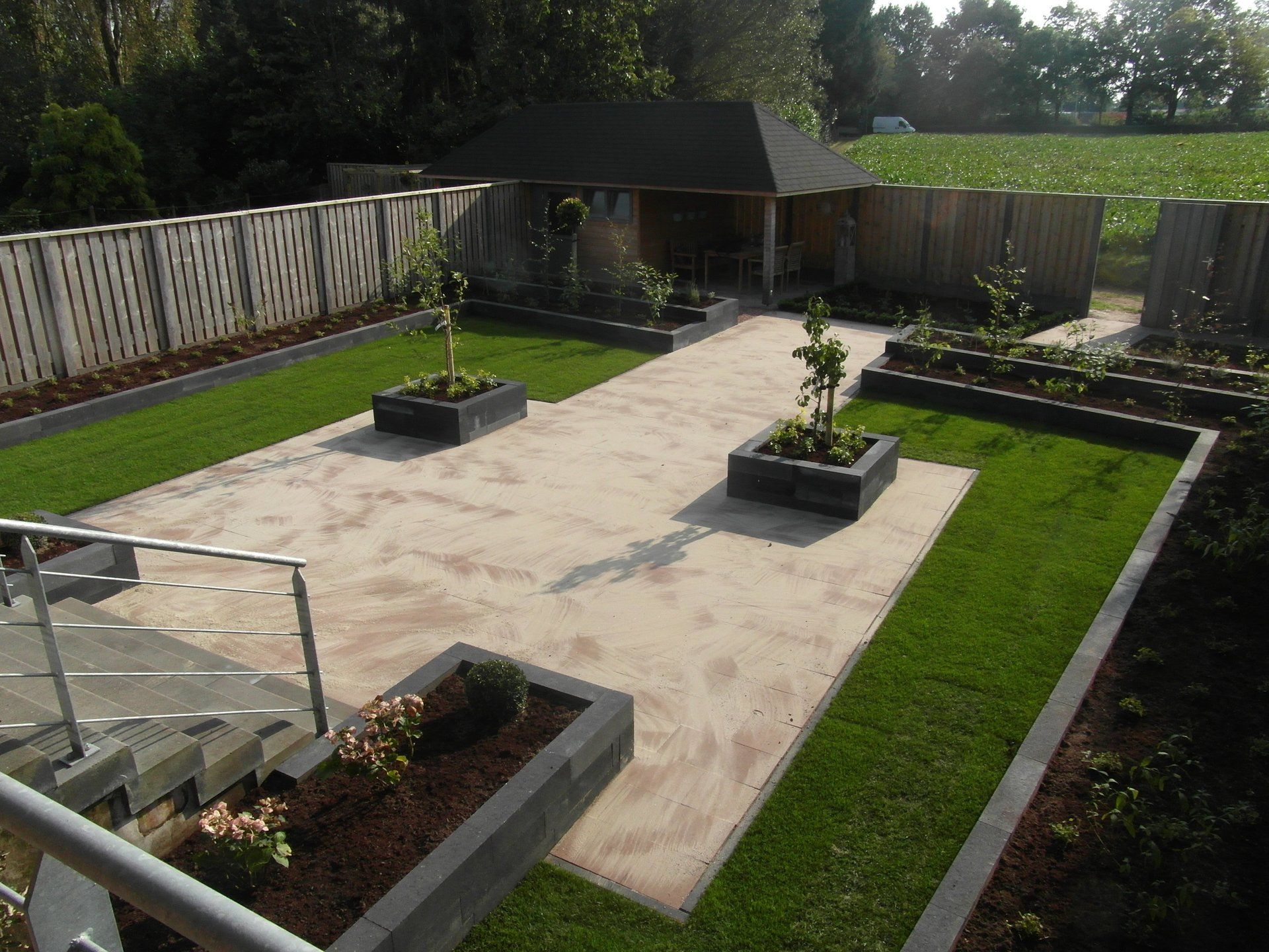 Toegankelijke binnentuin met verhoogde plantenbakken, een verhard middenpad en groene gazonranden.