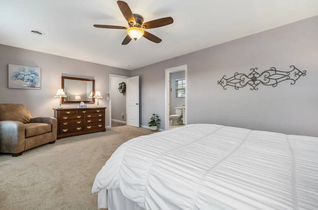 A bedroom with a bed , dresser , chair and ceiling fan.