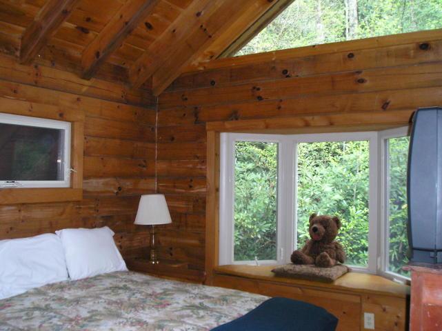 A bedroom in a log cabin with a teddy bear sitting on a window sill