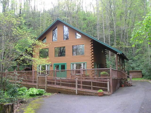 A large log cabin with a green roof is surrounded by trees.