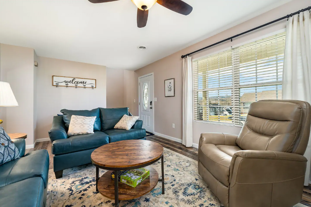 A living room with a couch , chair , coffee table and ceiling fan.