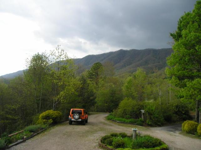 A jeep is parked on the side of a dirt road with mountains in the background.