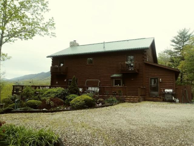 A large log cabin with a green roof is surrounded by trees and gravel.