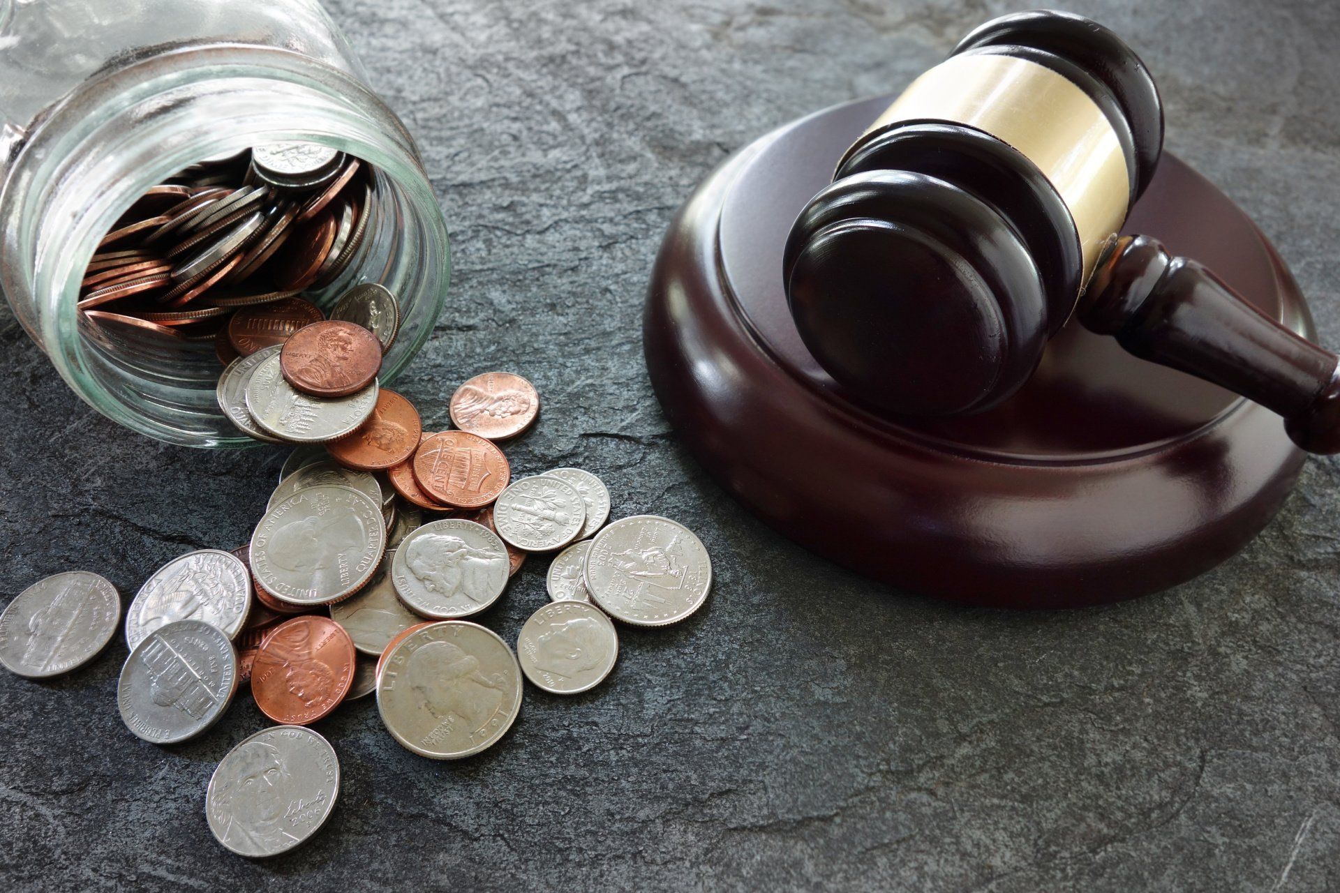 Coins spilled from a jar beside a judge’s gavel on a dark surface