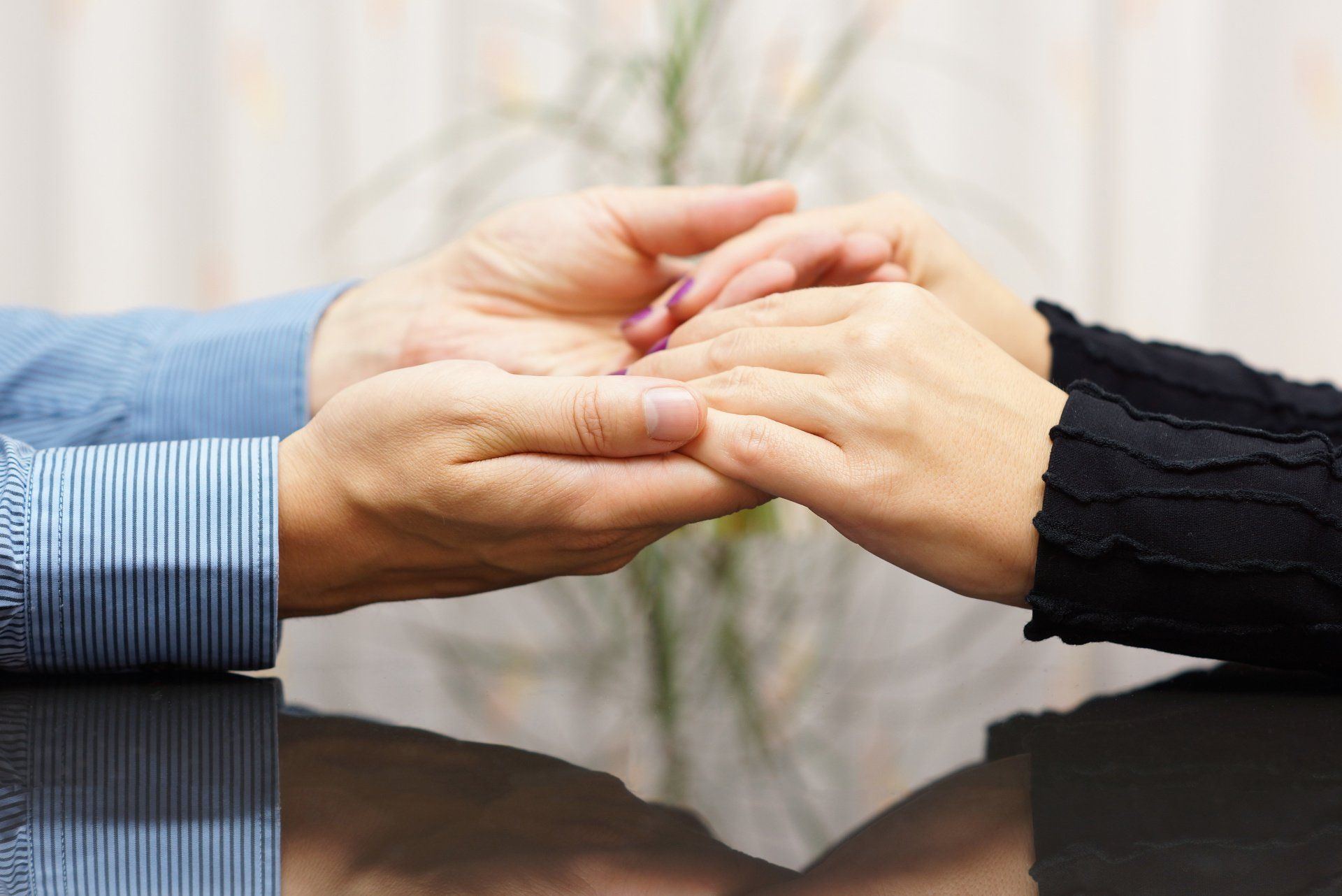 Hands gently holding fingers across a table, with blue and black sleeves visible.