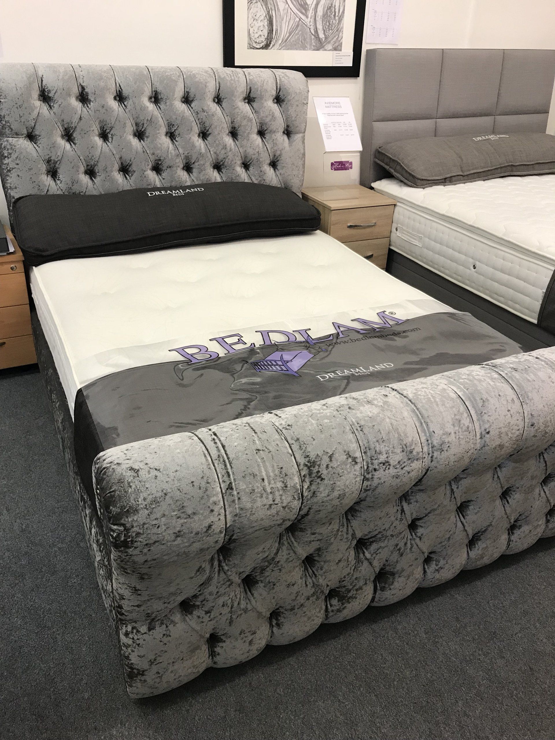 A bed with a tufted headboard is sitting next to a mattress in a store.