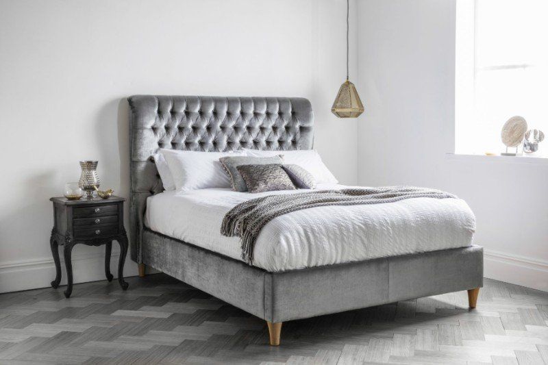 A bed with a tufted headboard is sitting in a bedroom next to a nightstand.