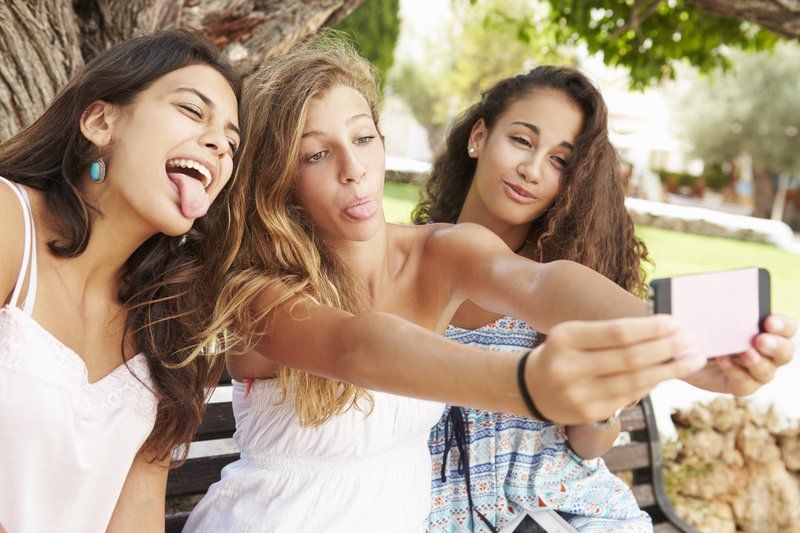 Three women making faces while taking a selfie outdoors.