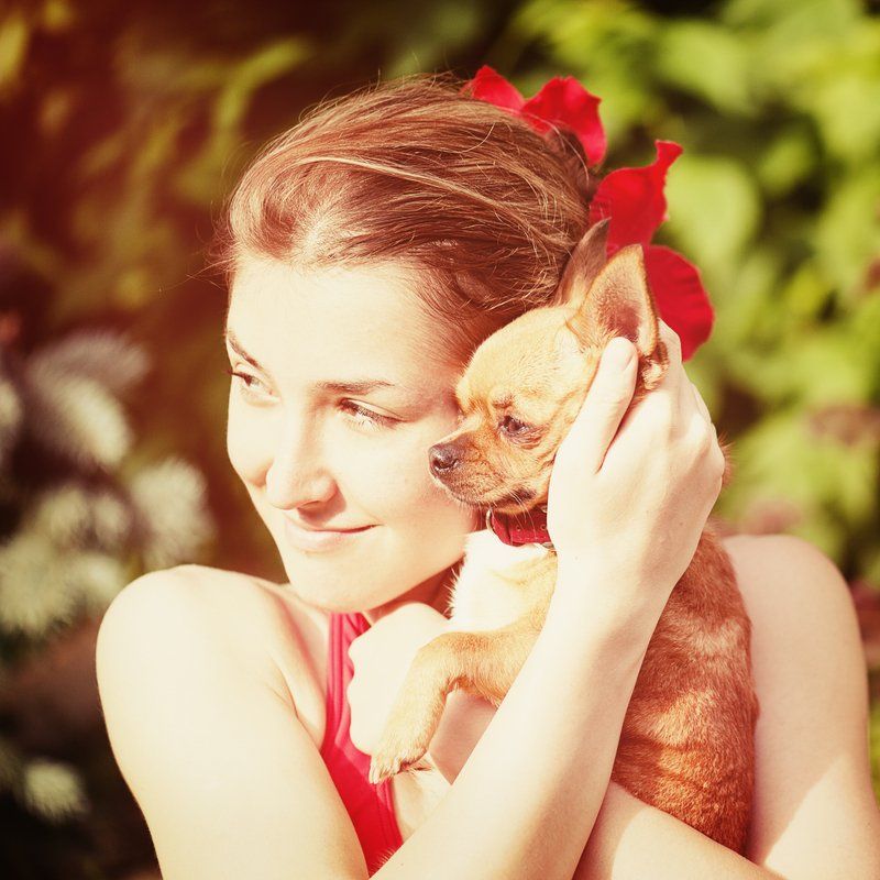 Woman embracing a small brown dog outdoors, wearing red, with a red bow in her hair.