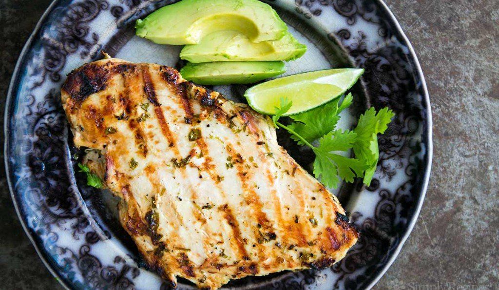 Grilled chicken breast with avocado, lime, and cilantro on decorative plate.