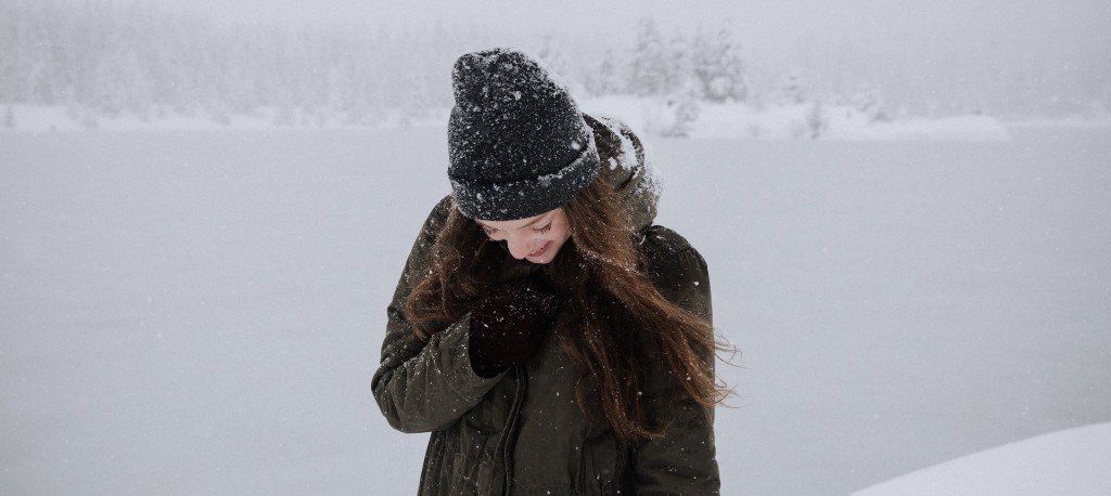 A person in a black beanie and coat stands in a snowy landscape, looking down.