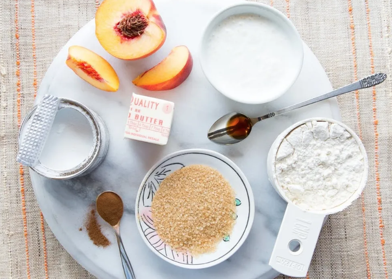 Ingredients for peach cobbler: peaches, sugar, flour, butter, cinnamon, and maple syrup.