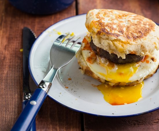 Breakfast sandwich on a white plate with a runny egg and a fork.