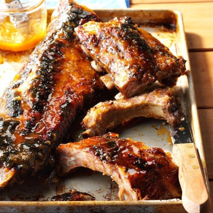 Cooked ribs in a baking pan, glistening with glaze, alongside a jar of sauce.