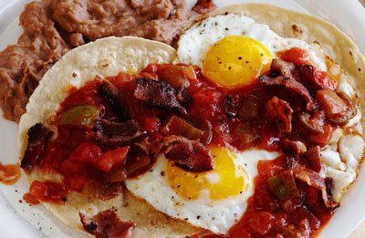 Plate of Mexican breakfast: fried eggs on tortillas, with salsa, bacon, and refried beans.