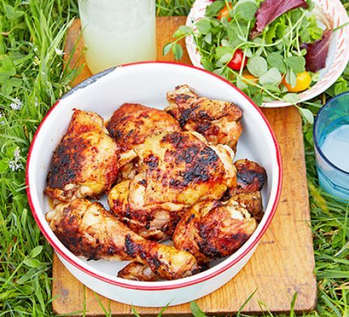 Grilled chicken in a bowl, with salad and lemonade on a wood board outdoors.