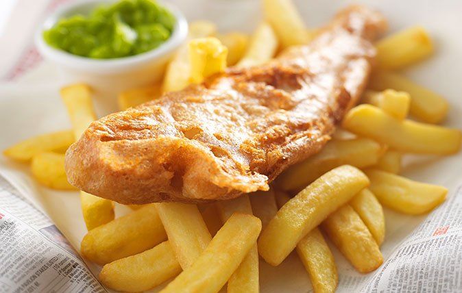 A close up of a plate of fish and chips on a newspaper.