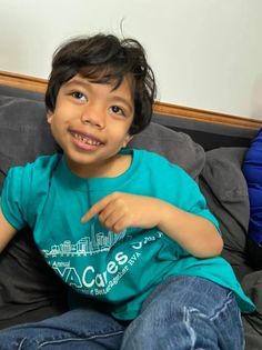 A young boy wearing a t-shirt that says acres is sitting on a couch