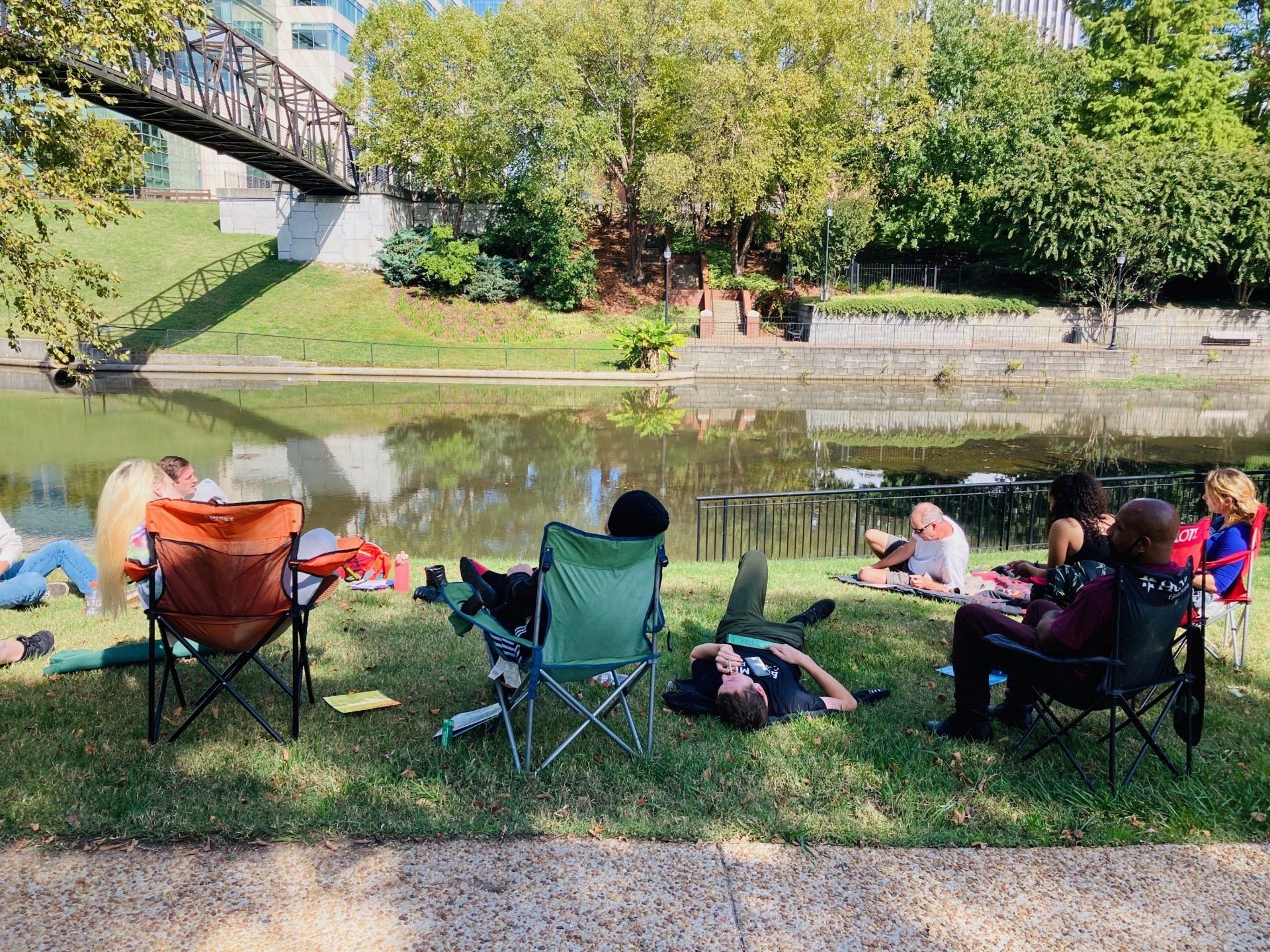 A group of people are sitting in folding chairs near a lake.
