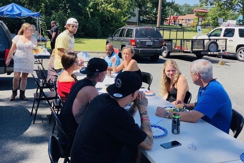 A group of people are sitting at a table in a parking lot.