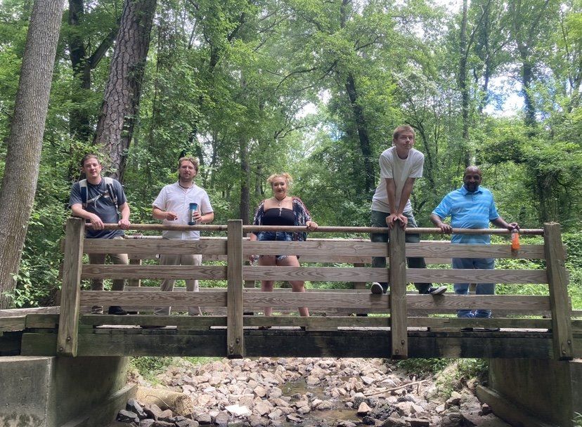A group of people are standing on a wooden bridge in the woods.