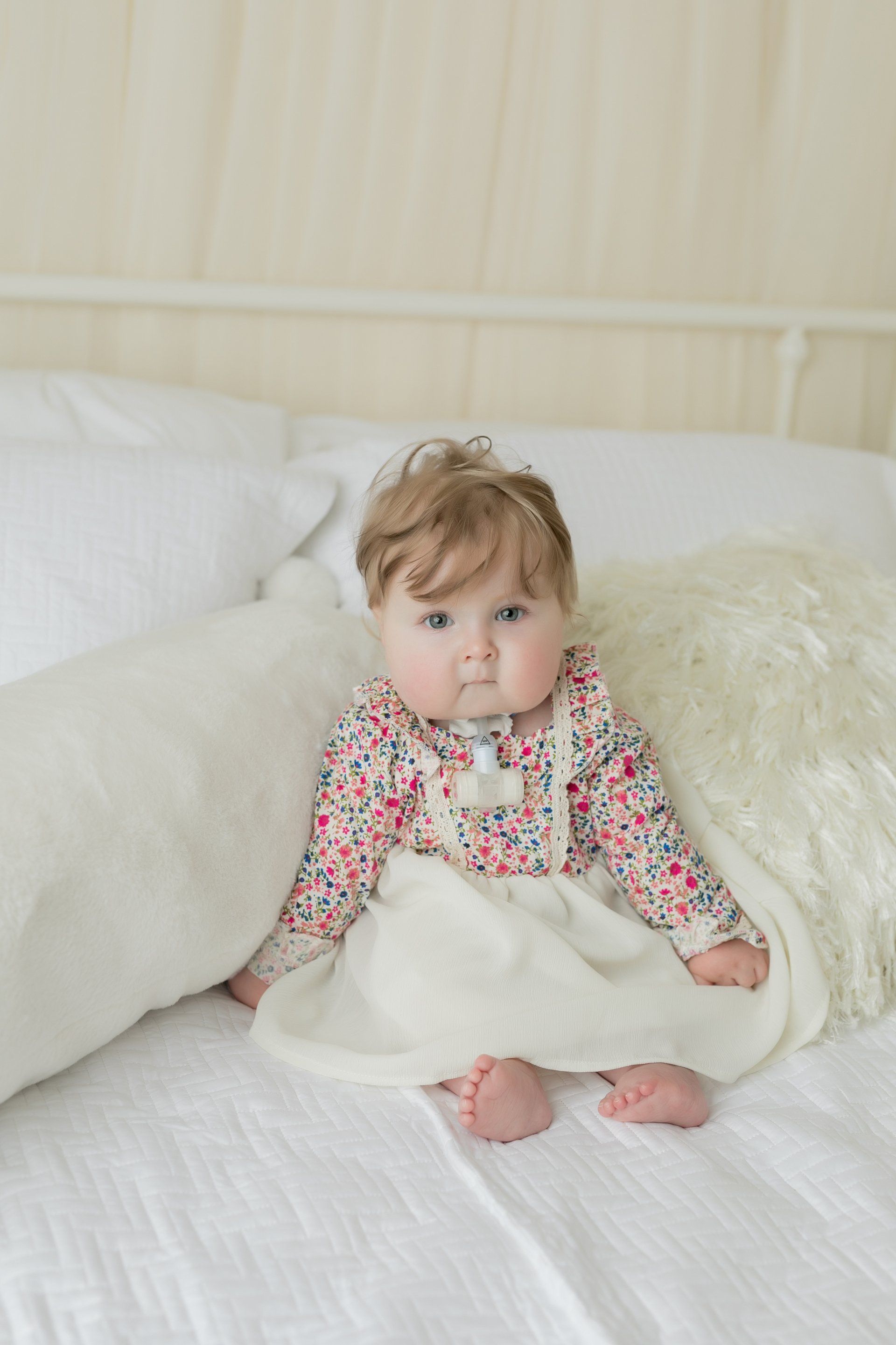 A baby girl in a dress is sitting on a bed.