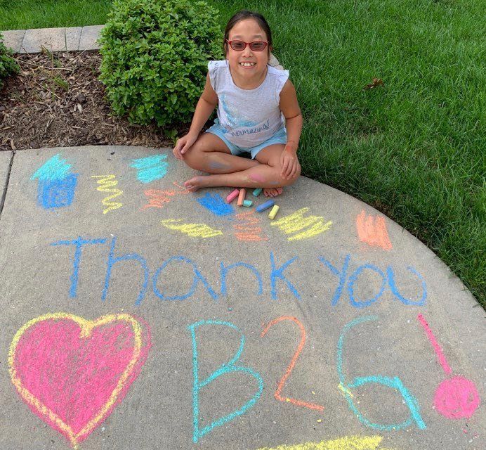 A little girl sits on a sidewalk with chalk drawings that say thank you b26