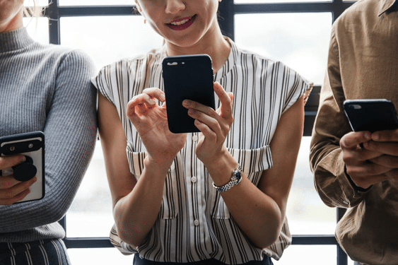 three people are standing next to each other looking at their cell phones
